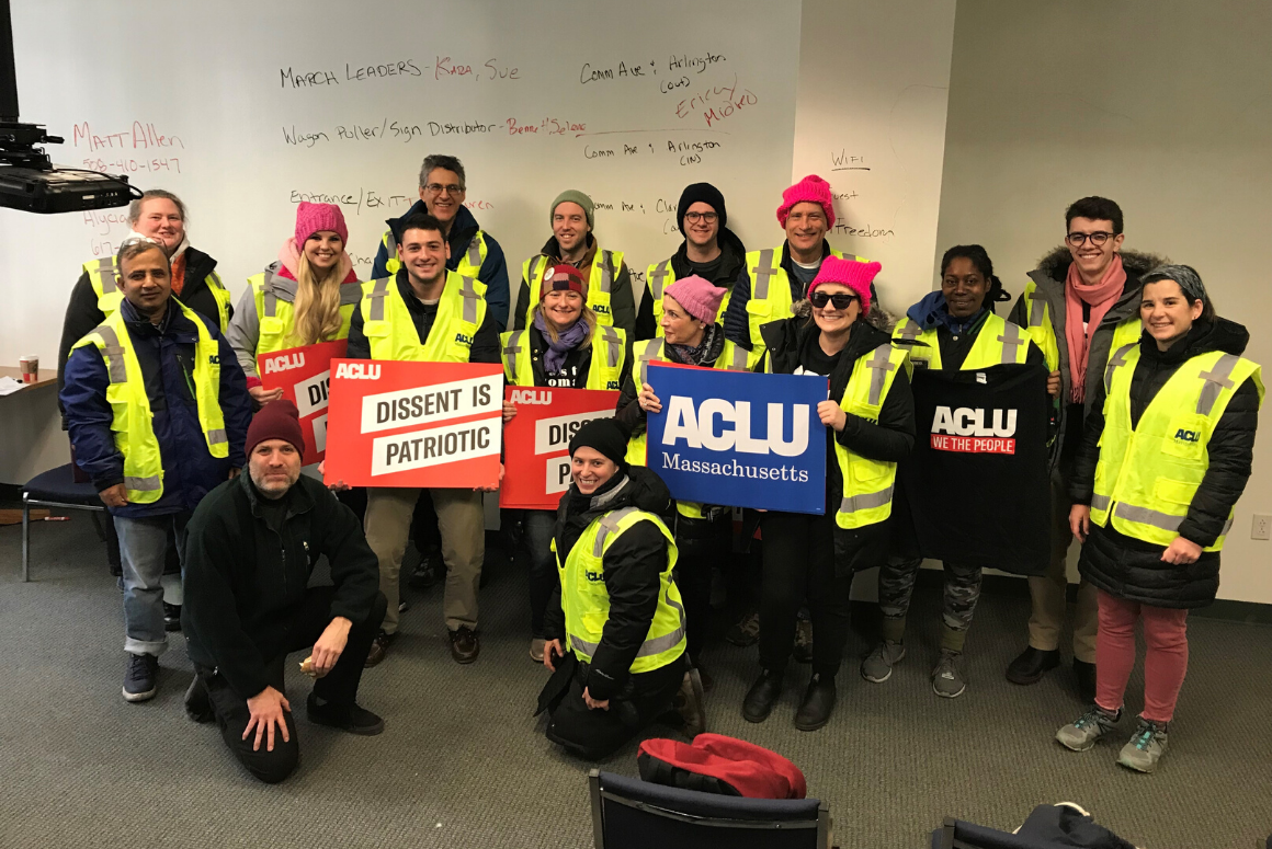 Volunteers in bright yellow ACLU vests hold ACLU signs